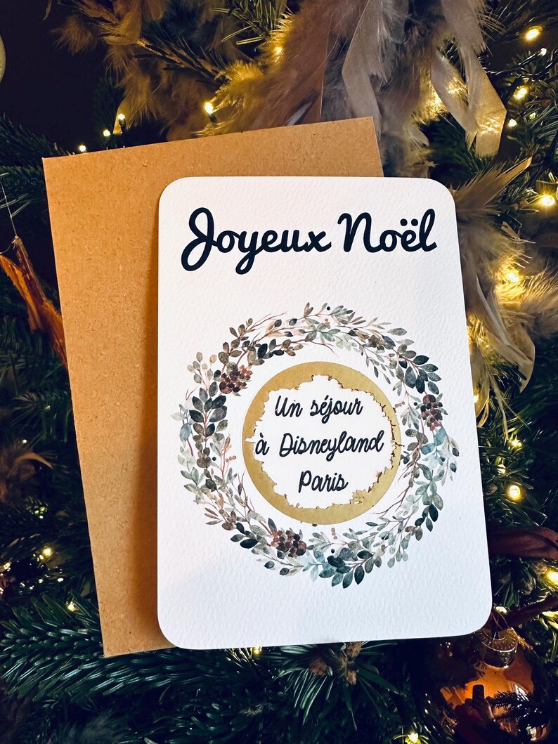 May include: A white card with a gold wreath and the words 'Joyeux Noël' and 'Un séjour à Disneyland Paris'.