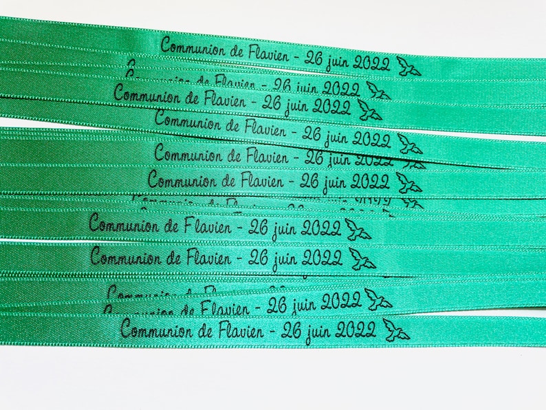 May include: Several green ribbons with black text that reads "Communion de Flavien - 26 juin 2022". Each ribbon has a small bird graphic. The ribbons are stacked on top of each other.