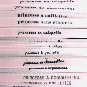 May include: Close-up of several pink ribbons with black text. The ribbons feature French phrases like "Princesse &agrave; paillettes" and "Princesse en chaussettes." The ribbons are likely for crafts or gift wrapping.
