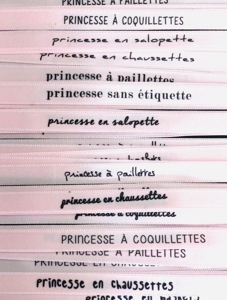 May include: Close-up of several pink ribbons with black text. The ribbons feature French phrases like "Princesse &agrave; paillettes" and "Princesse en chaussettes." The ribbons are likely for crafts or gift wrapping.