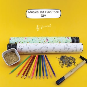 K&ouml;nnte beinhalten: Ein DIY-Musikkit mit einer wei&szlig;en Pappr&ouml;hre, einer gr&uuml;n-wei&szlig;en Pappr&ouml;hre, einer Sch&uuml;ssel Reis, einem Hammer, N&auml;geln und Buntstiften. Die R&ouml;hren haben ein Schmetterlings- und Blumendesign. Der Text auf der wei&szlig;en R&ouml;hre lautet "Musical Kit RainStick DIY".