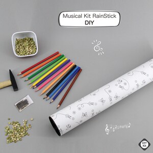 K&ouml;nnte beinhalten: Ein DIY-Musikalisches Regenstick-Set mit einer wei&szlig;en Pappr&ouml;hre, bunten Bleistiften, einer kleinen T&uuml;te mit Erbsen, einem Hammer und N&auml;geln. Die R&ouml;hre hat ein schwarz-wei&szlig;es Schmetterlingsdesign und der Text "Musical Kit RainStick DIY" befindet sich auf einem wei&szlig;en Rechteck.