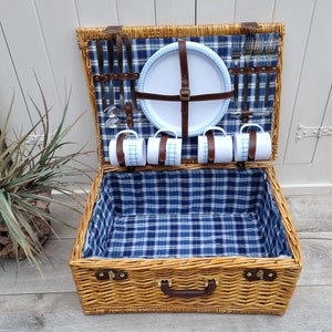 May include: A wicker picnic basket with a blue and white checkered lining. The basket is open and contains a white plate, four mugs, and silverware.