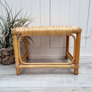 Könnte beinhalten: Ein naturgeflochtener Rattanhocker mit rechteckiger Oberseite und einem einfachen, stabilen Gestell. Der Hocker ist hellbraun und hat ein natürliches, rustikales Aussehen.