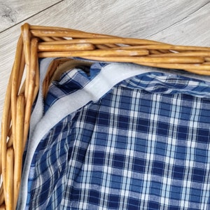 May include: A wicker basket lined with a blue and white plaid fabric. The fabric has a white border around the edge.