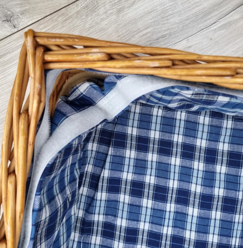 May include: A wicker basket lined with a blue and white plaid fabric. The fabric has a white border around the edge.