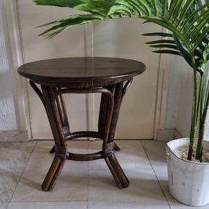 Op de afbeelding: Een ronde bijzettafel van gevlochten rotan in donkerbruin met een rond blad. De tafel heeft een eenvoudig ontwerp met vier poten en een ronde basis.
