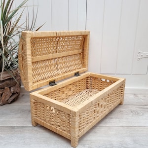 May include: A natural woven wicker storage box with a hinged lid. The box is open and the inside is visible. The box is made of natural woven wicker and has a light brown color.