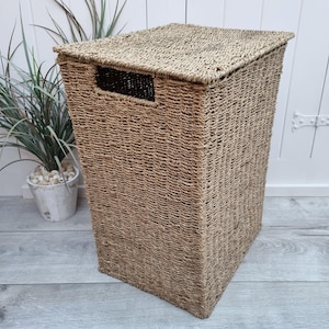 May include: A natural woven storage basket with a lid. The basket is made of a light brown material and has a rectangular shape.