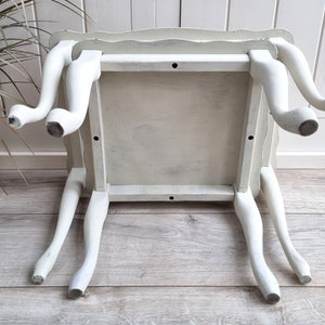 May include: White painted wooden side table with a scalloped edge and four legs. The table is distressed and has a rustic look.