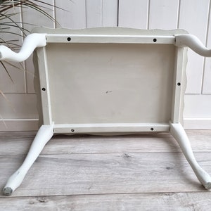 May include: White painted wooden table with four legs. The table has a scalloped edge and is turned upside down to show the underside of the table top.