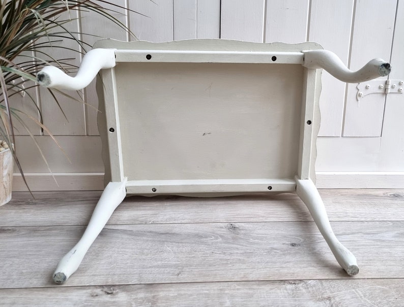 May include: White painted wooden table with four legs. The table has a scalloped edge and is turned upside down to show the underside of the table top.