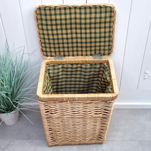 May include: A rectangular wicker storage basket with a hinged lid. The interior and lid lining feature a green and yellow plaid pattern. The basket is open, revealing the plaid interior.