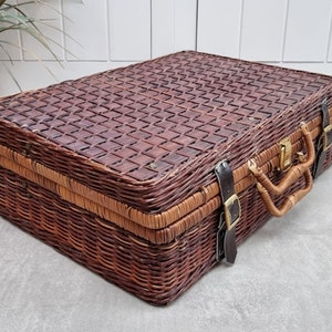 May include: A brown wicker suitcase with leather straps and a brass latch. The suitcase has a woven pattern on the top and a handle on the side.