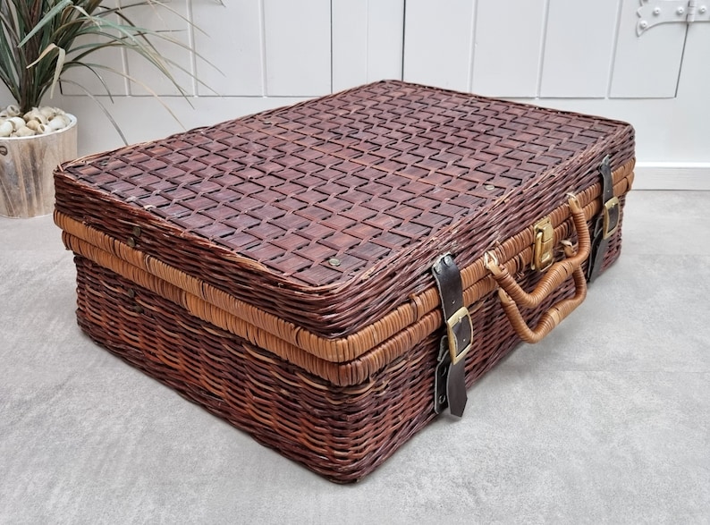 May include: A brown wicker suitcase with leather straps and a brass latch. The suitcase has a woven pattern on the top and a handle on the side.