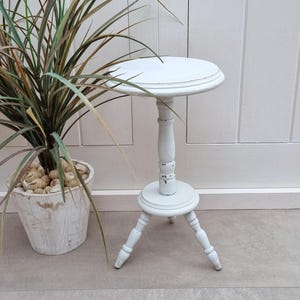 May include: White wooden side table with a round top and three legs. The table has a distressed finish and is painted white.