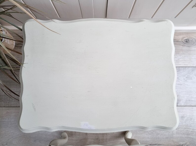May include: A white painted table with a scalloped edge and a distressed finish. The table has a simple design and is perfect for a small space.