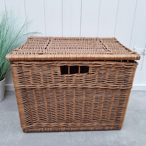 May include: A large, brown wicker storage basket with a lid. The basket is woven with a tight, even pattern and has a rectangular shape.
