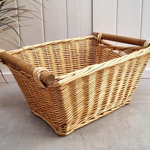 May include: A rectangular wicker basket with two wooden handles. The basket is made of natural woven wicker and has a light brown colour.
