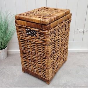 May include: A large, rectangular wicker laundry basket with a lid. The basket is made of natural brown wicker and has a woven pattern. The lid is hinged and has a handle.