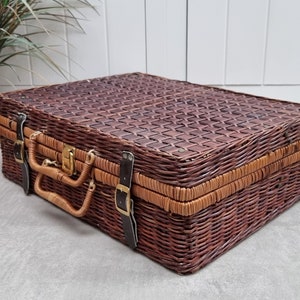 May include: A brown wicker suitcase with leather straps and a brass latch. The suitcase has a woven pattern and is closed.