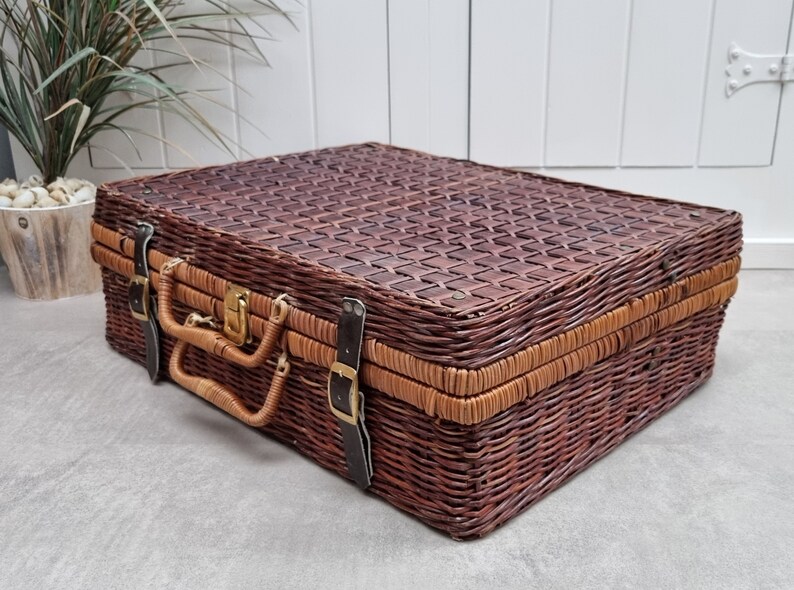May include: A brown wicker suitcase with leather straps and a brass latch. The suitcase has a woven pattern and is closed.