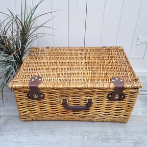 May include: A woven wicker basket with a brown leather handle and brass accents. The basket is closed and has a lid.
