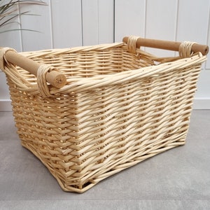 Op de afbeelding: Een natuurlijke geweven rieten mand met twee houten handvatten. De mand is rechthoekig en heeft een lichtbruine kleur.
