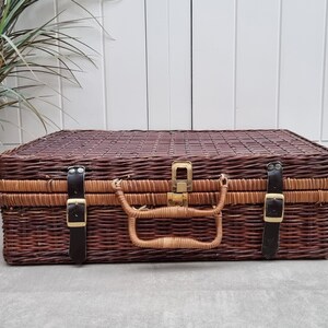May include: A brown wicker suitcase with leather straps and a brass latch. The suitcase has a woven pattern and is closed.