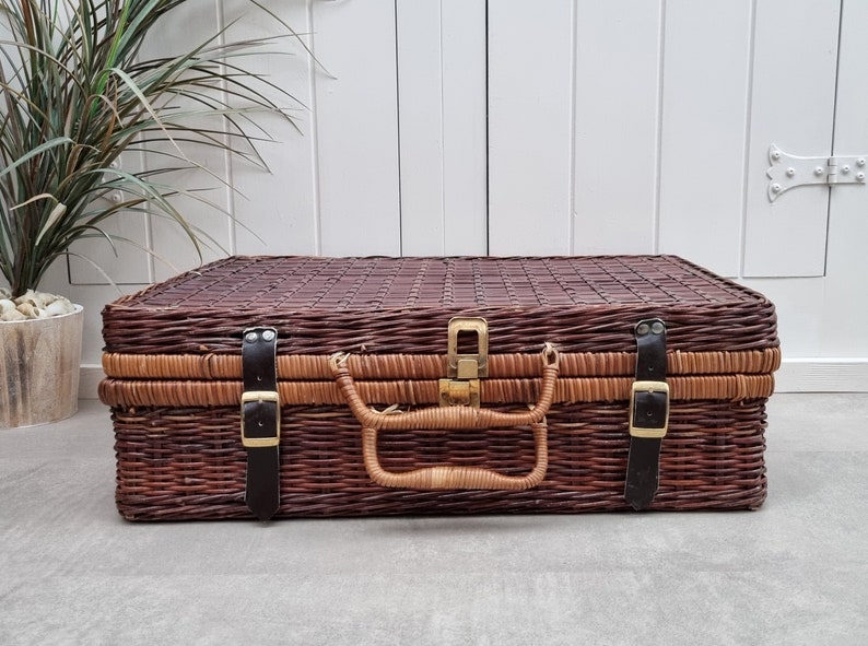 May include: A brown wicker suitcase with leather straps and a brass latch. The suitcase has a woven pattern and is closed.