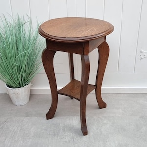 May include: A dark brown wooden side table with a round top and a lower shelf. The table has three legs with curved details.