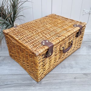 May include: A woven wicker basket with a brown leather handle and brass hardware. The basket has a rectangular shape and is made of natural materials.