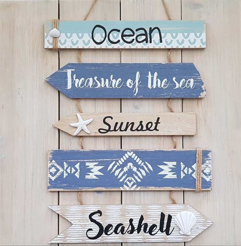 May include: Four wooden signs with a nautical theme. The signs are painted in shades of blue and white and feature the words "Ocean", "Treasure of the Sea", "Sunset", and "Seashell".