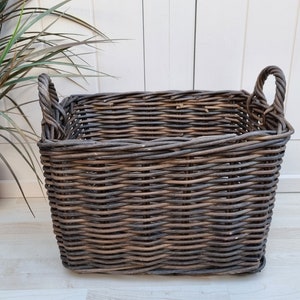 May include: A large, square wicker basket with two handles. The basket is made of natural woven wicker with a dark brown stain. The basket is empty.
