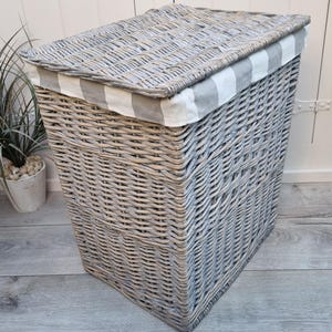 May include: A gray wicker laundry basket with a white and gray striped fabric lid. The basket is sitting on a wooden floor.