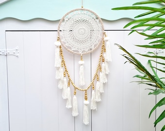 Puede incluir: Atrapasueños de crochet blanco con cuentas de madera y borlas blancas colgando de una puerta de madera blanca.