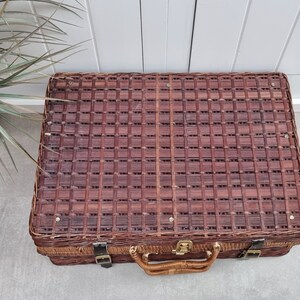 May include: A brown wicker suitcase with a woven pattern and a leather handle. The suitcase has two metal clasps and a brass lock.