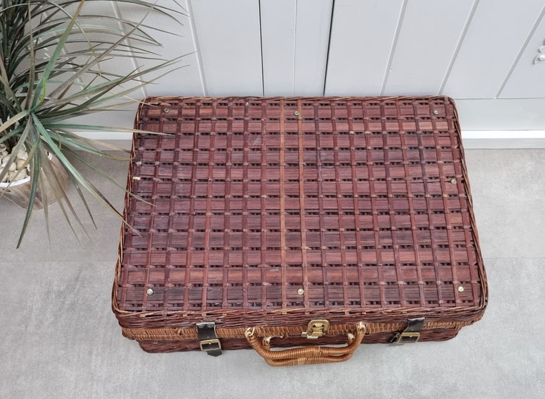 May include: A brown wicker suitcase with a woven pattern and a leather handle. The suitcase has two metal clasps and a brass lock.