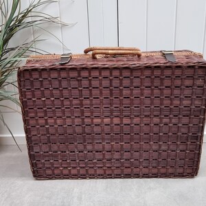 May include: A brown wicker picnic basket with a woven lid and leather straps. The basket has a rectangular shape and is made of natural materials.