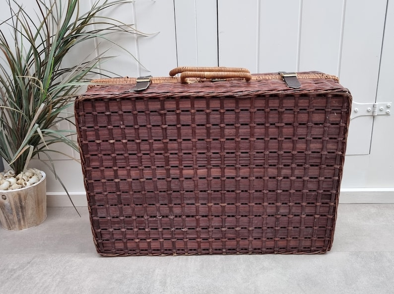 May include: A brown wicker picnic basket with a woven lid and leather straps. The basket has a rectangular shape and is made of natural materials.