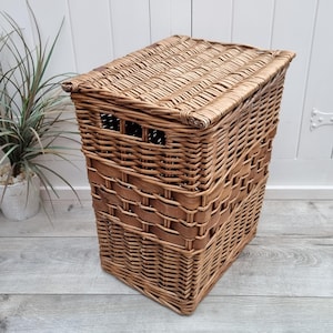 May include: A large, rectangular wicker laundry basket with a lid. The basket is made of natural brown wicker and has a woven pattern. The lid is hinged and has a leather strap.