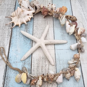 Könnte beinhalten: Dekorative Anordnung mit Muscheln und einem weißen Seestern auf einer blau-weiß gestrichenen Holzoberfläche. Die Muscheln sind mit Schnur zu einem Halbkreis verbunden. Der Seestern liegt in der Mitte.