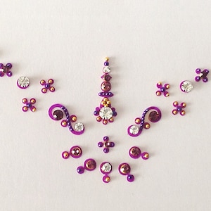 May include: Purple and gold temporary body jewellery with a floral design. The jewellery is made up of small, sparkly stones and is perfect for adding a touch of sparkle to any outfit.