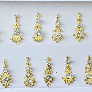 May include: A sheet of 24 gold and white rhinestones in various designs. The rhinestones are arranged in two rows of 12.