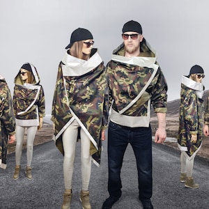 May include: Five people are wearing camouflage jackets with white accents. The jackets have a unique design with a large hood and a wrap-around style. The jackets are worn over black pants and jeans. The people are standing on a paved road with a mountain range in the background. The text "FLASHION WEAR" is visible in the top left corner of the image.
