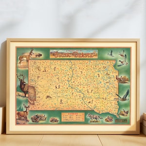 May include: A framed vintage map of South Dakota, featuring illustrations of wildlife and geographical details. The map has a green border and a tan background, with the state's name in a decorative font. The frame is a light wood color.