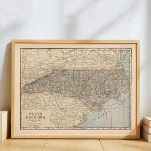 Könnte beinhalten: Eine gerahmte Vintage-Karte von North Carolina mit detaillierten Straßen, Städten und geografischen Merkmalen. Die Karte befindet sich in einem hellen Holzrahmen und enthält den Text "North Carolina". Die Karte ist beige mit roten und grünen Akzenten.