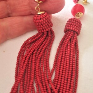 Peut inclure: Boucles d'oreilles pendantes à pompons rouges perlées avec des accents dorés. Les boucles d'oreilles comportent un groupe de petites perles en haut, une grosse perle ronde et une longue gland de petites perles.