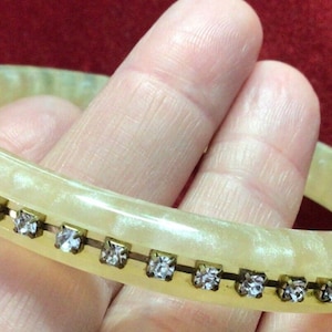 May include: A white bangle bracelet with a row of clear rhinestones set in gold tone metal.
