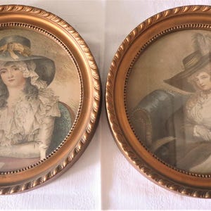 May include: Two antique framed portraits of women in hats. The round frames are gold-colored with a rope-like texture. The portraits depict women in period clothing, with soft colors and details. The artwork is set against a neutral background.
